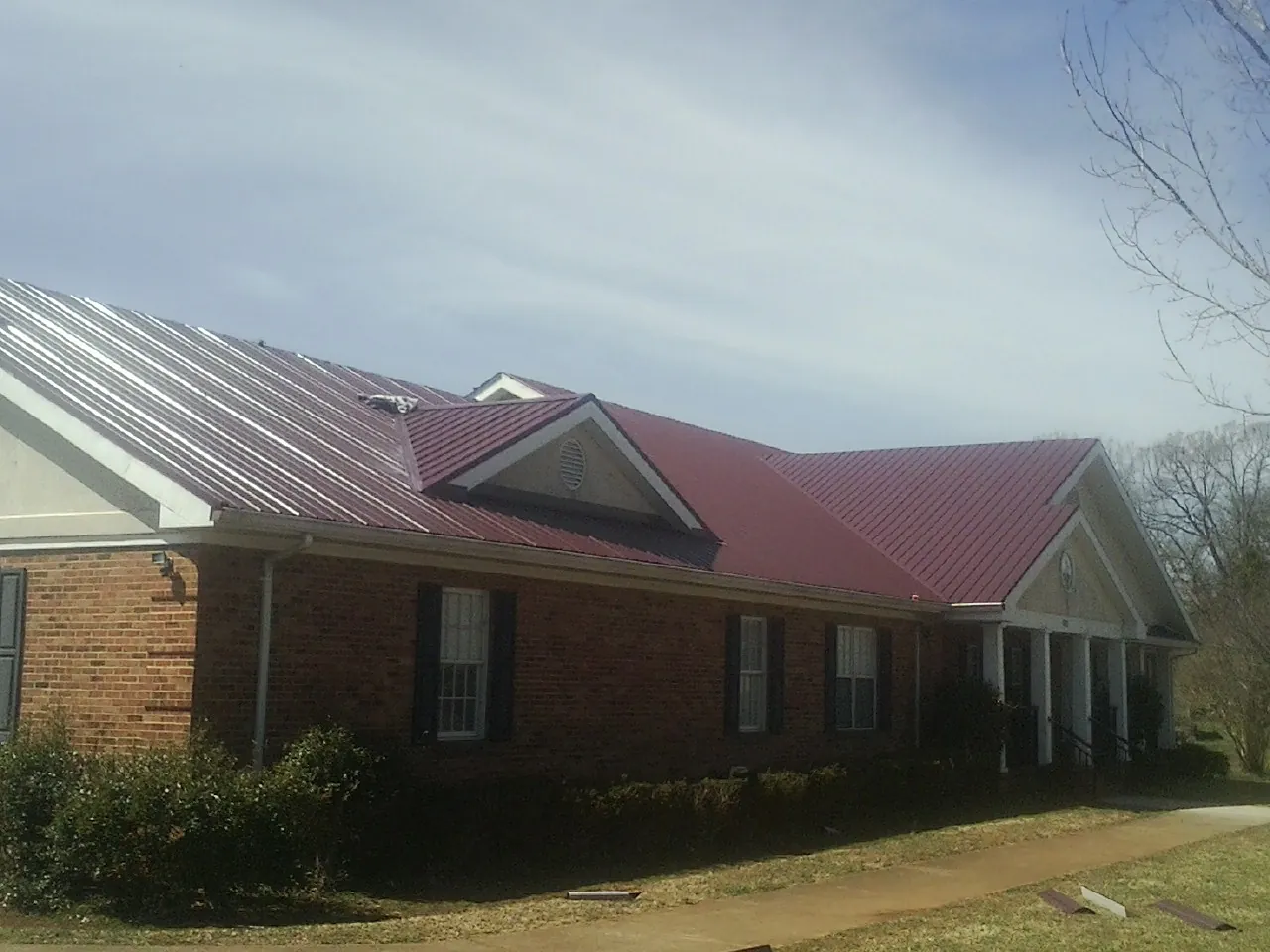 Red metal roof with gabled entries on a long brick building, from a Hail Damage Roof Repair job in Hyde Park